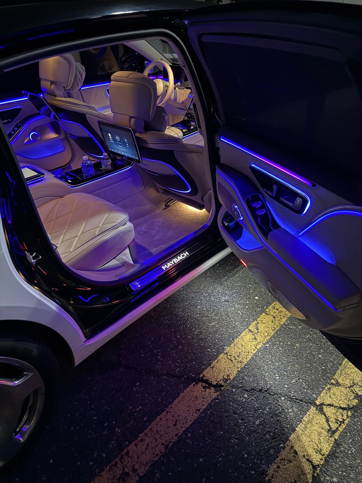 Luxury car interior with blue ambient lighting, open door, quilted leather seats, and modern dashboard display at night
