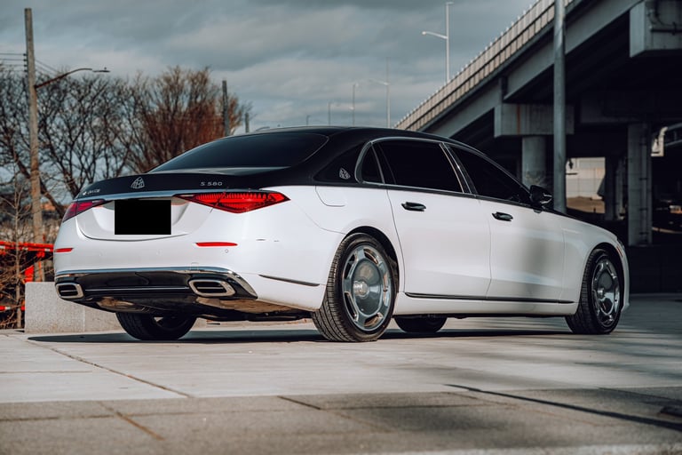 White luxury sedan photographed from the rear three-quarter angle in an urban setting with overpass visible in background