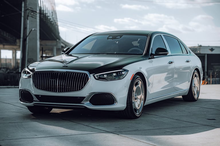 White luxury sedan with vertical grille parked on a concrete lot near industrial buildings