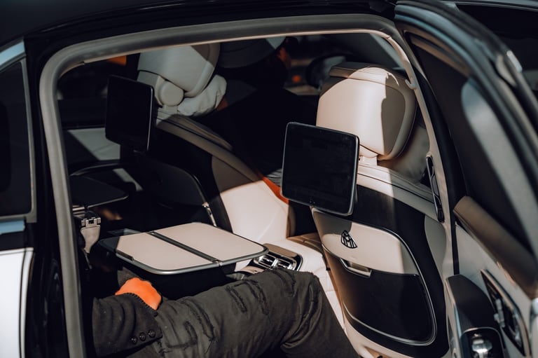 Interior of a car showing white and black seats with headrest monitors and a digital display, viewed through the side window